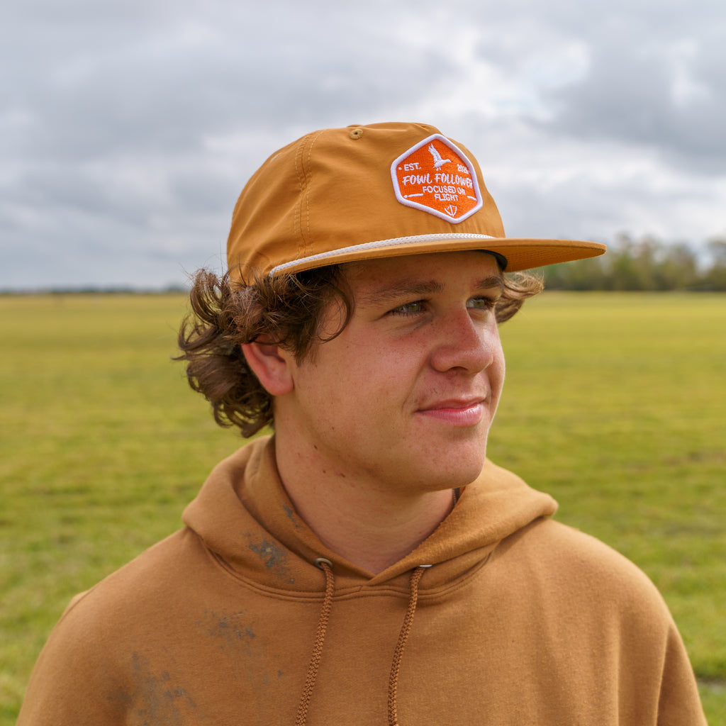A young man wearing a Fowl Follower Crush Rope Hat and a brown hoodie.